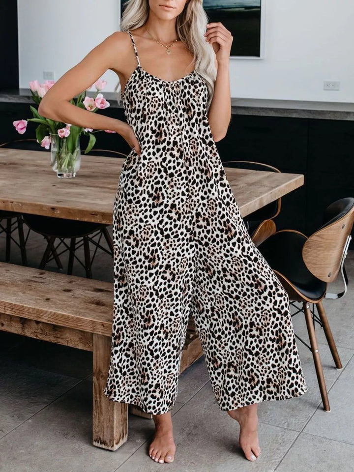Leopard print jumpsuit with spaghetti straps, hands on hips beside a table