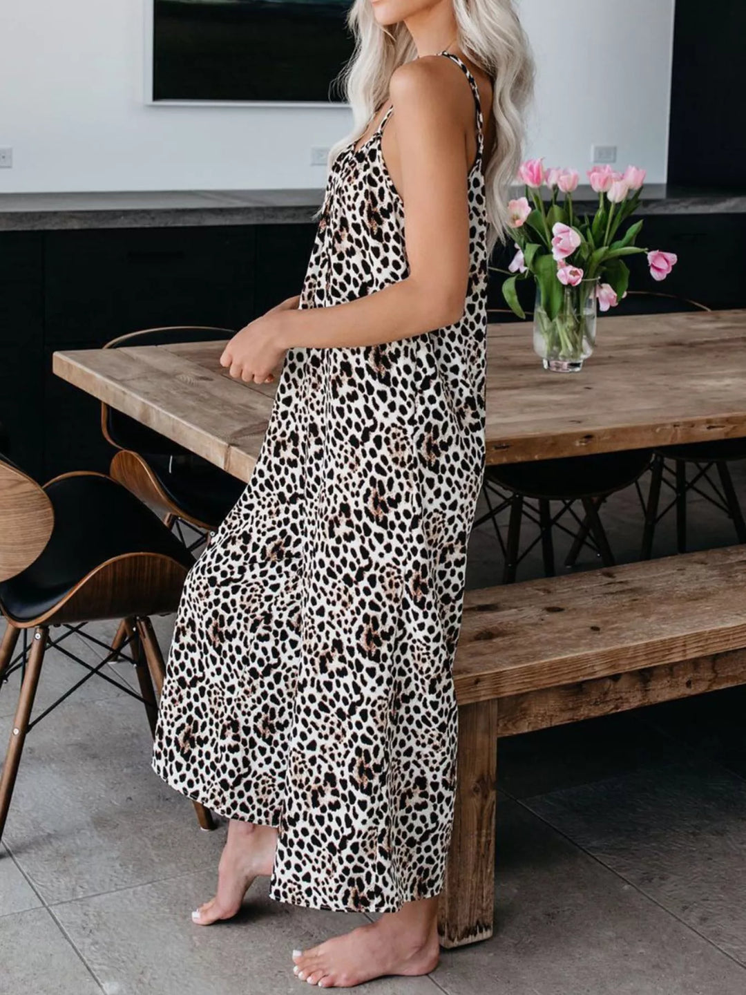Side view of the leopard print jumpsuit, barefoot beside a dining table