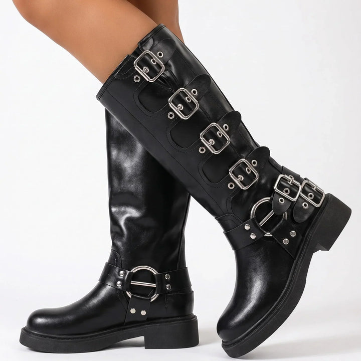 Model wearing the black knee high moto boots with buckle straps and ankle harness