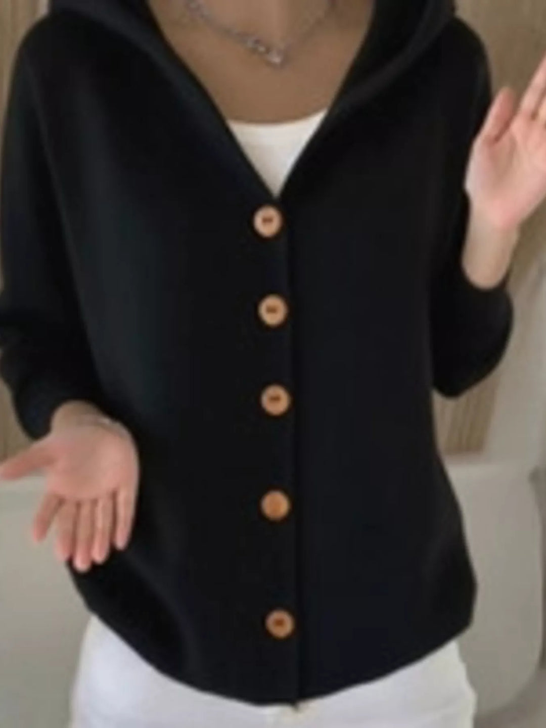 Black hooded button front cardigan worn with white pants and a hand gesture