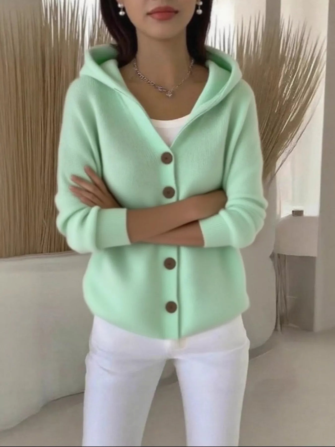 Mint green hooded cardigan worn with arms crossed over white pants