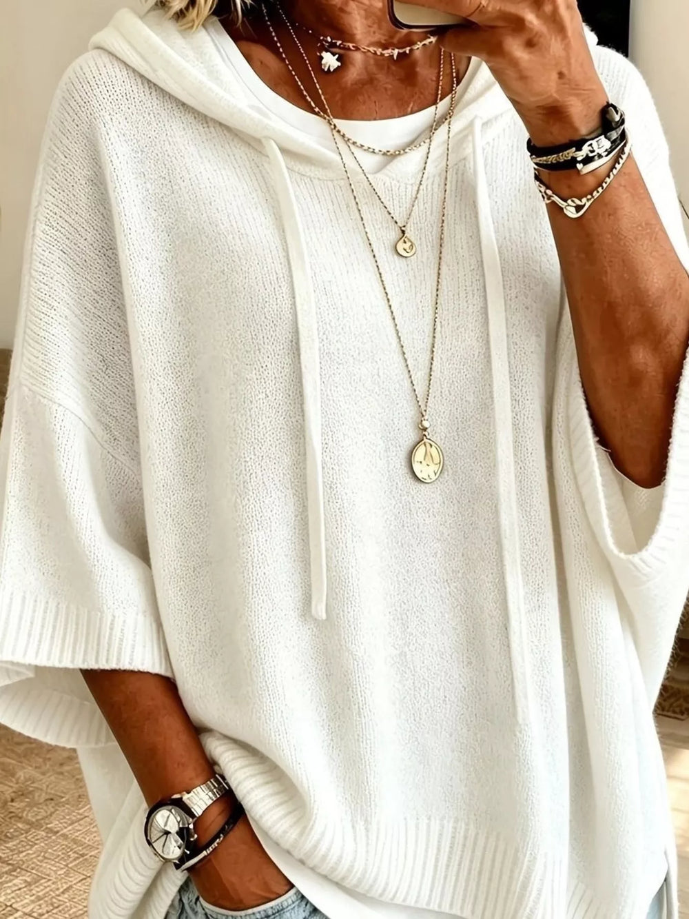 Close-up of the white hooded knit sweater drawstrings and layered necklaces