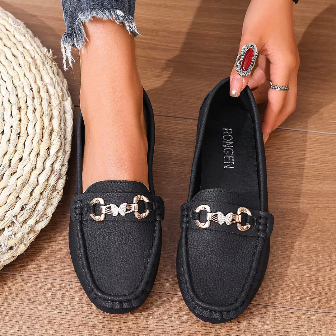 Pair of black moccasin flats with gold-tone buckles on a wood floor