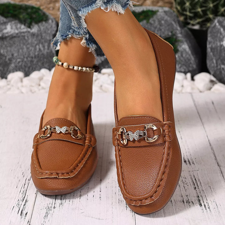 Cognac slip on loafers with a gold-tone buckle, worn outdoors with jeans