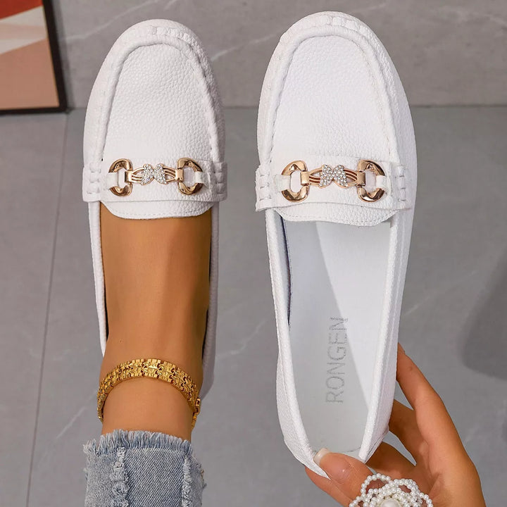 Pair of white loafers with gold-tone buckles, top view with an insole shown