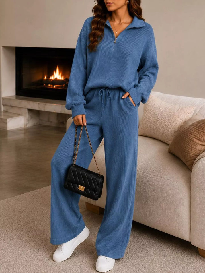 Dusty blue lounge set with quarter zip top, wide leg pants and black bag