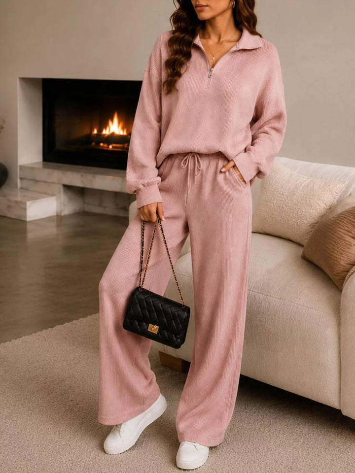 Dusty pink lounge set, standing by a fireplace with a quilted bag