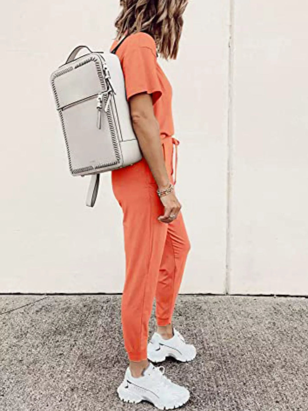 Coral tee and jogger set seen from the side, carrying a white backpack