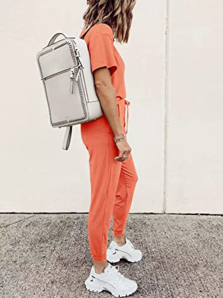 Coral tee and jogger set seen from the side, carrying a white backpack