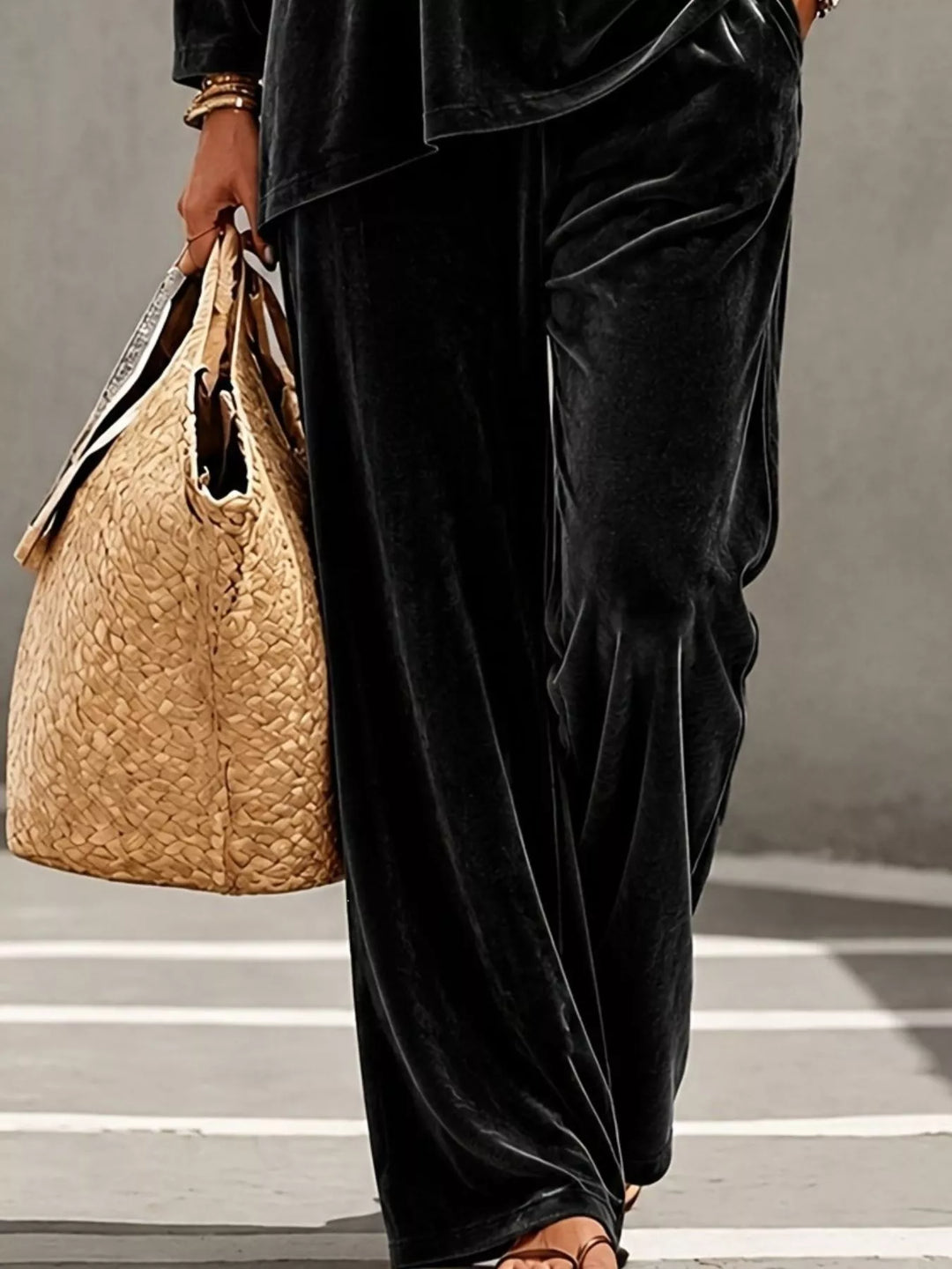 Black velvet wide leg pants beside a woven tote, lower body view