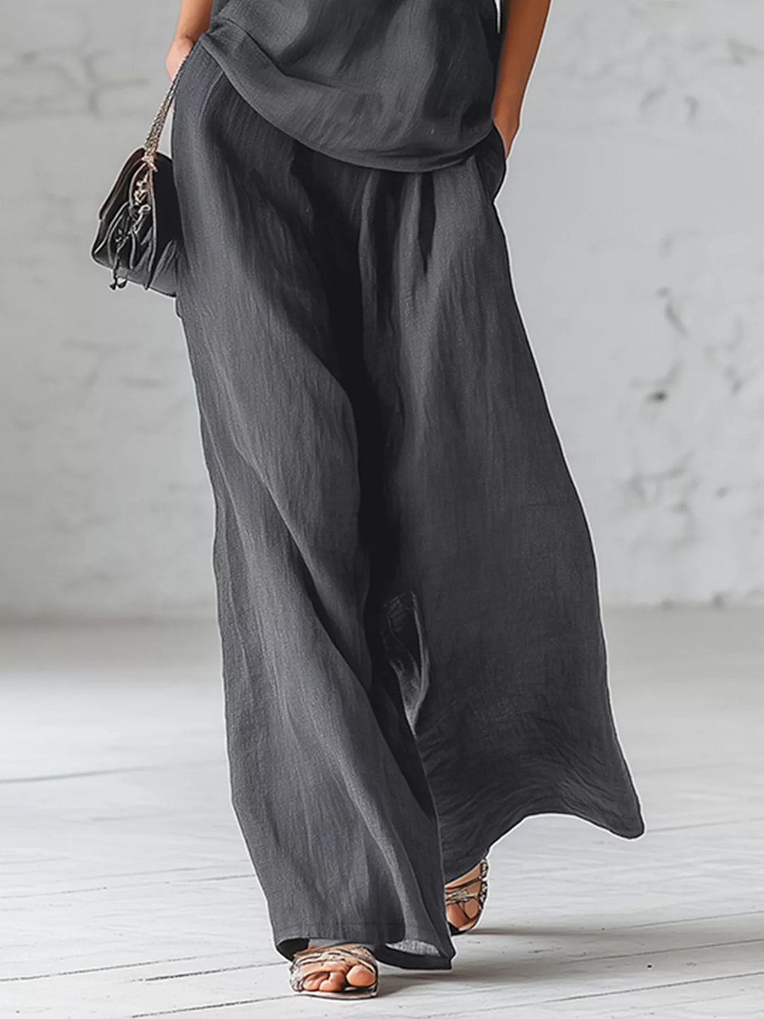 Charcoal wide leg pants walking pose with a small black bag