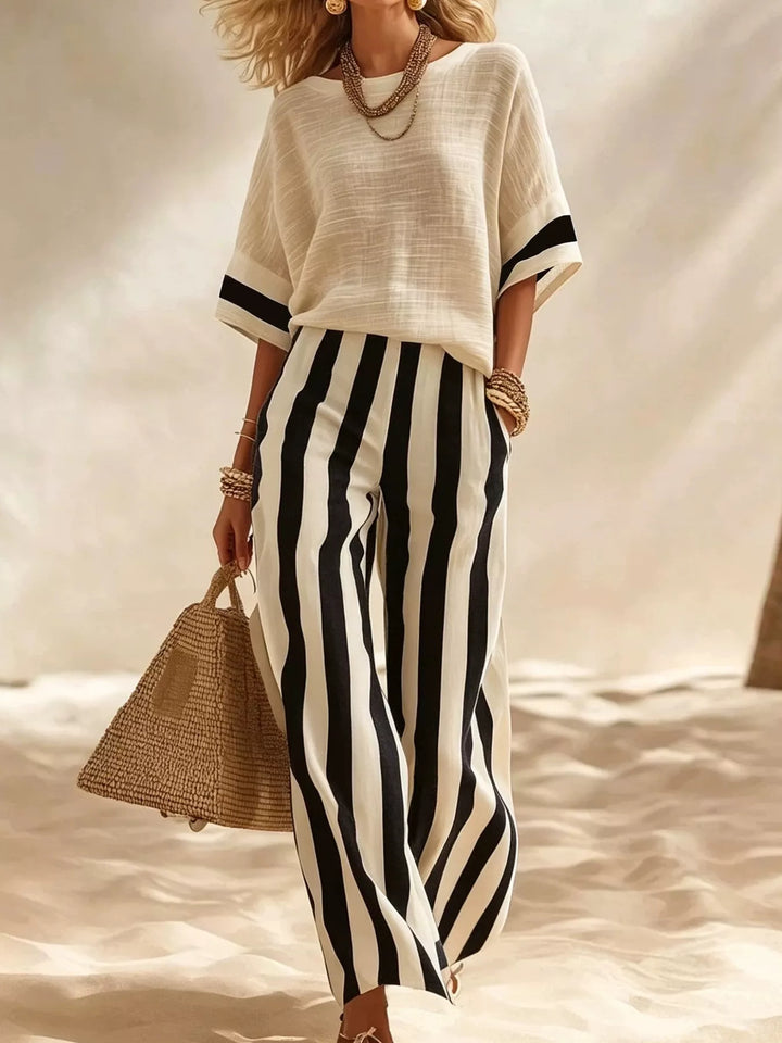Black striped wide leg pants and cream top set, walking with a straw tote