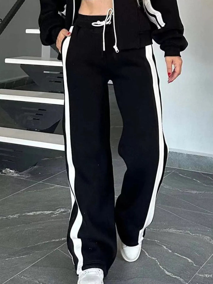 Black tracksuit pants with white side stripe and drawstring waist, walking pose
