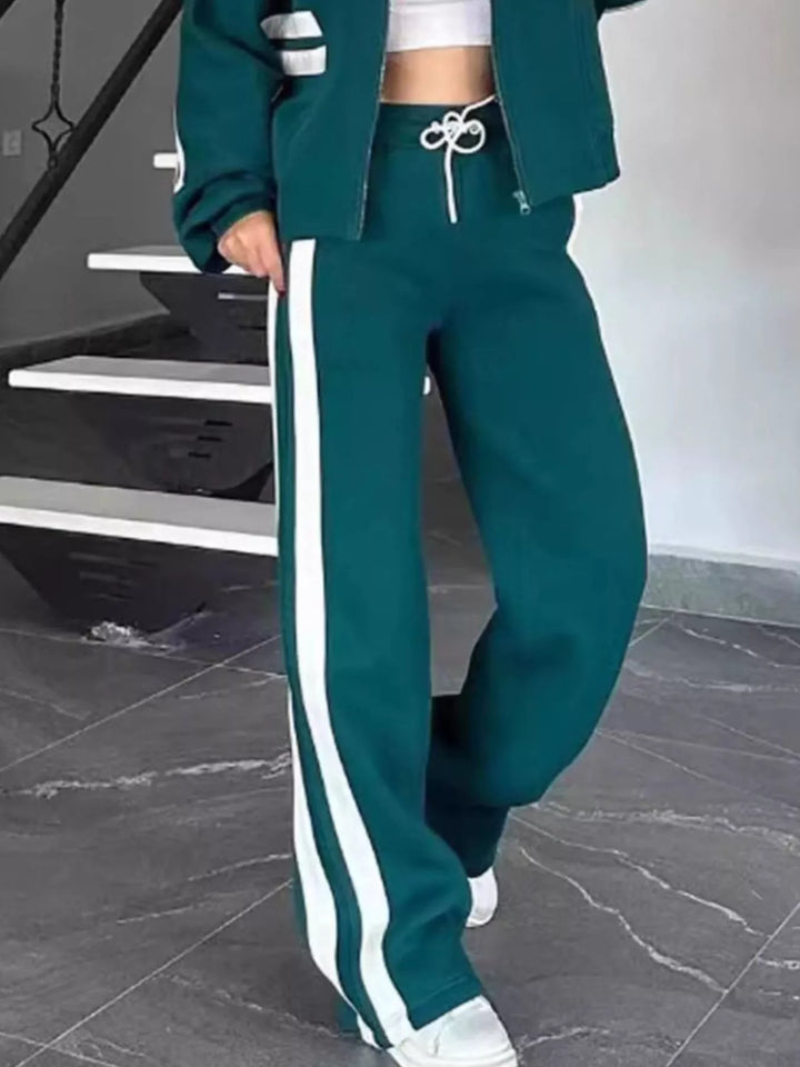 Teal tracksuit pants with white side stripe, stepping forward in sneakers