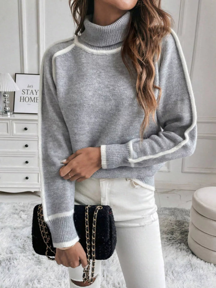Gray raglan sleeve sweater worn with white pants and a black quilted bag