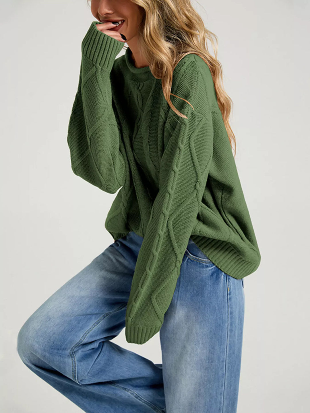 Forest green cable knit sweater in a playful side pose with wide leg jeans