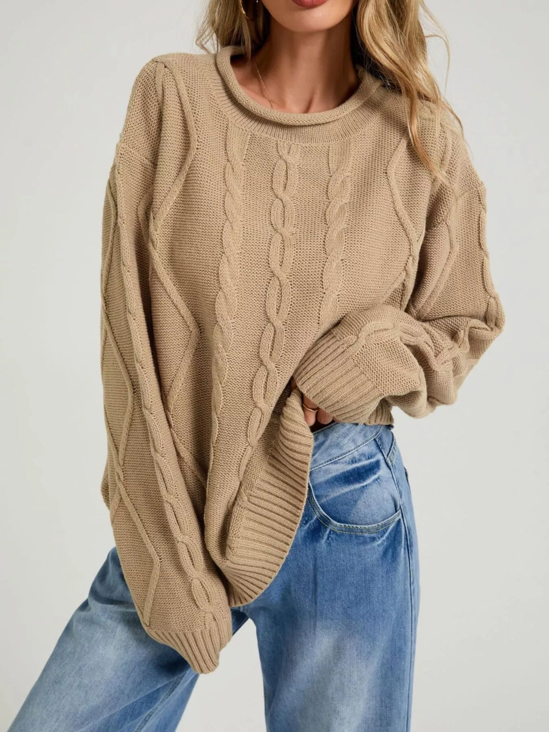 Tan oversized cable knit sweater with rolled neck, hand tucked in jeans