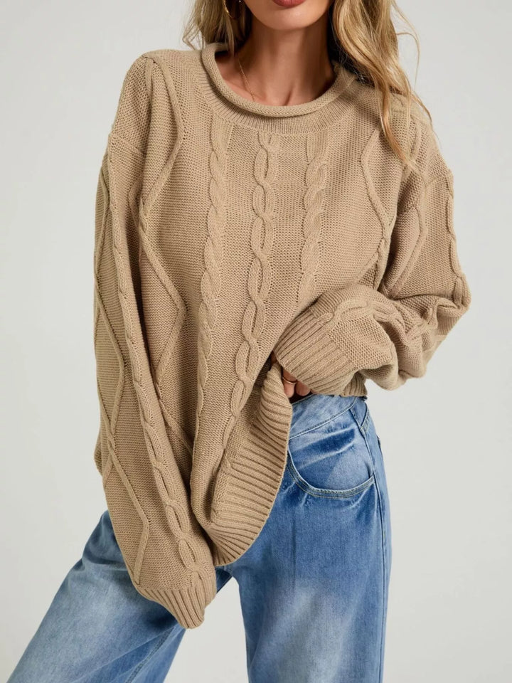 Tan oversized cable knit sweater with rolled neck, hand tucked in jeans