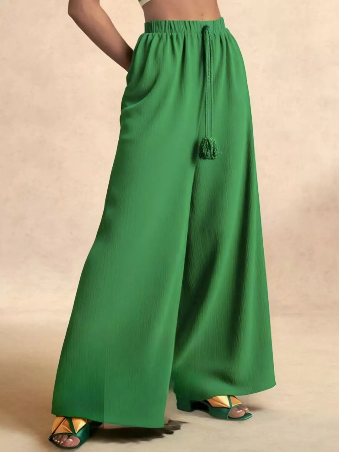Green extra wide flowy pants, three quarter angle with hand on hip