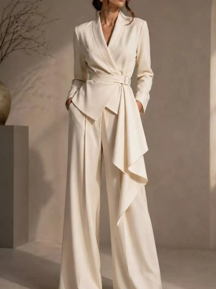 Beige belted wrap blazer pant suit with draped front, standing against a neutral wall