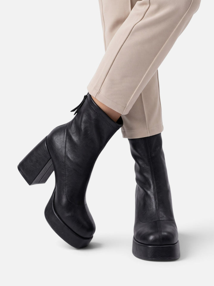 Model wearing black platform ankle boots with cream pants