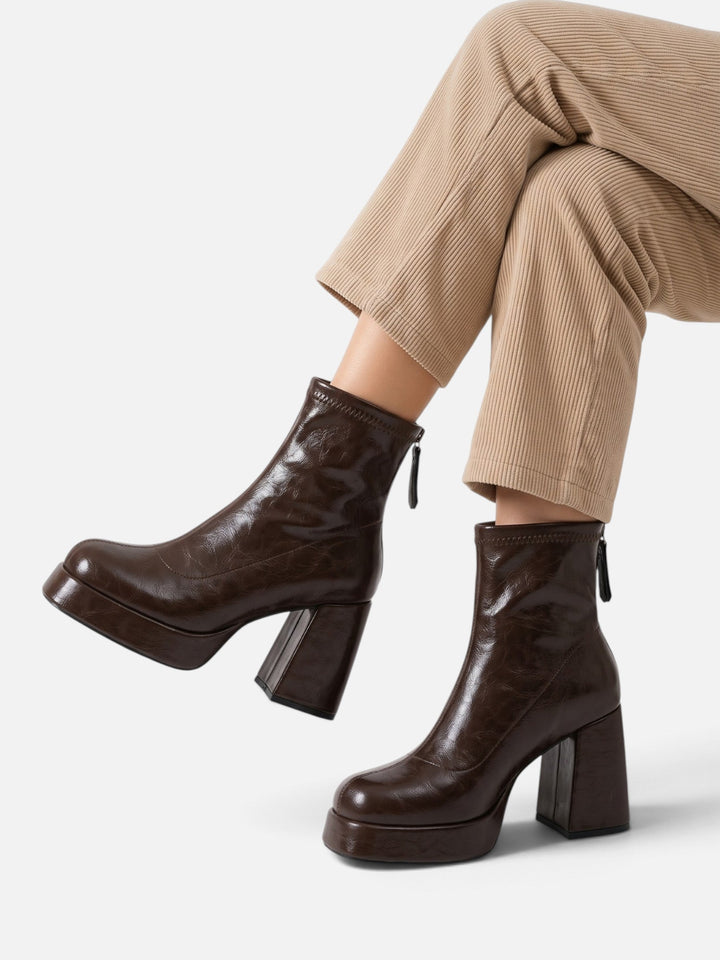 Dark brown platform ankle boots worn with crossed legs and beige pants