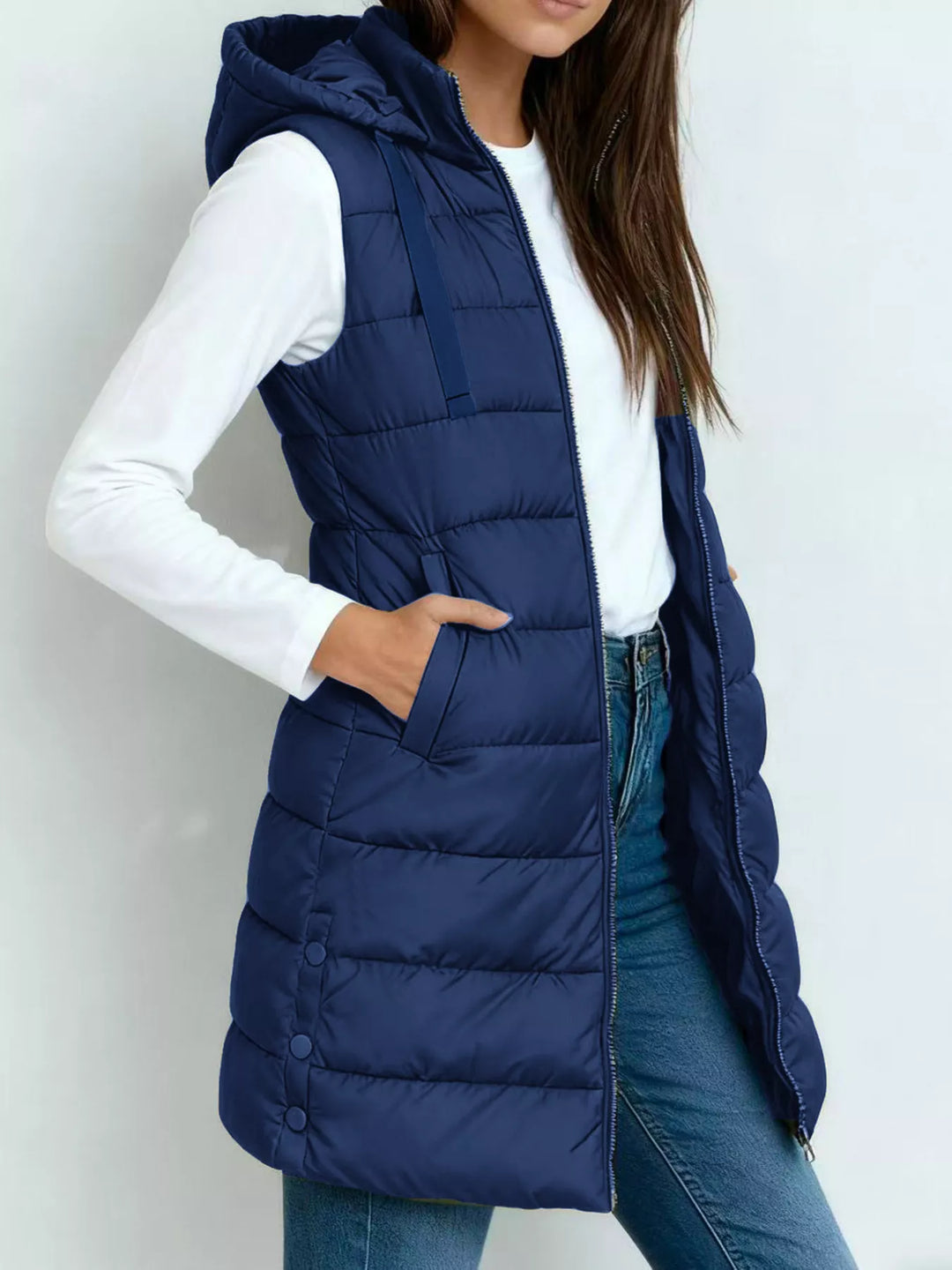 Deep blue longline puffer vest with hood and hand in pocket, over a white long sleeve