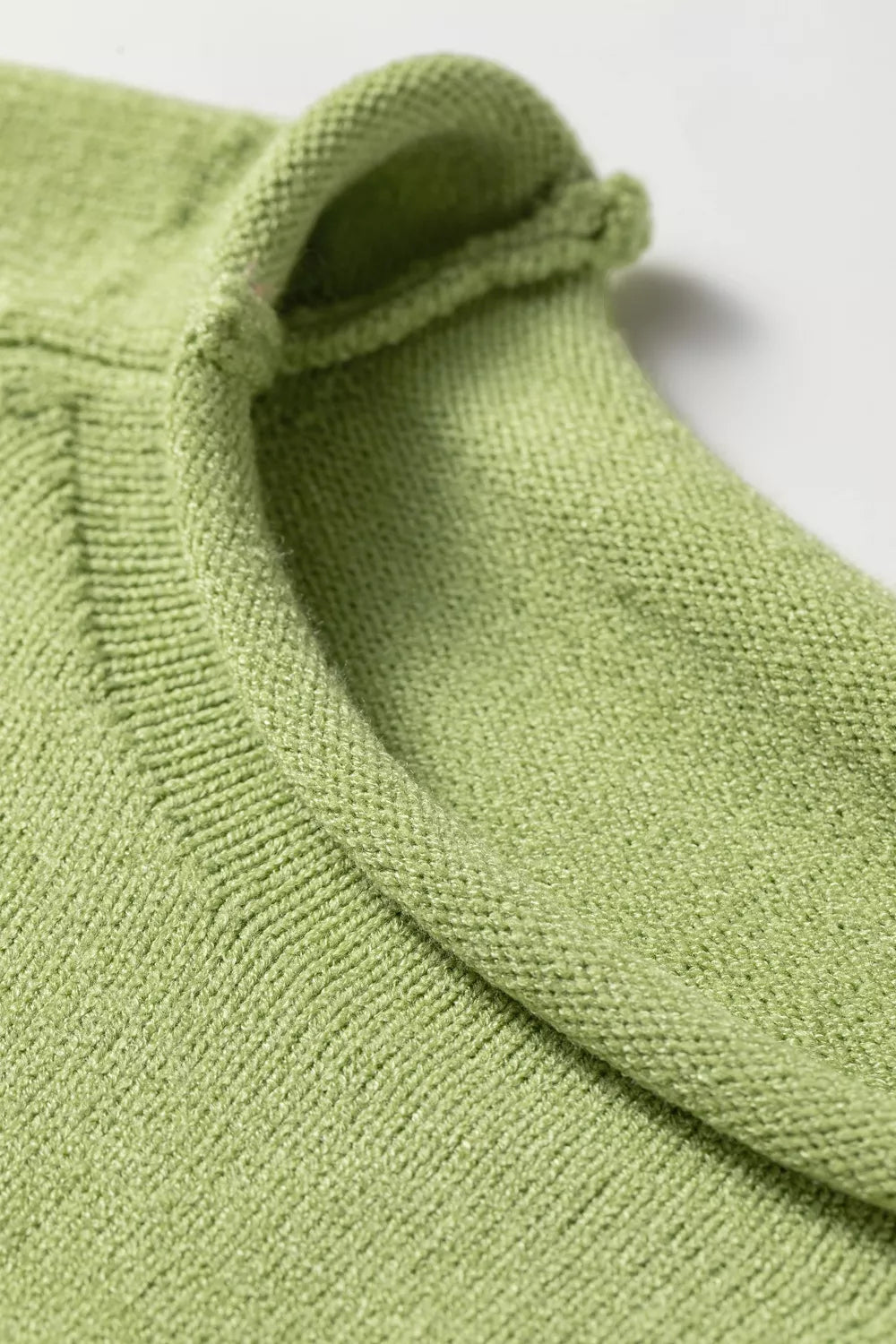 Close-up of the rolled crew neck edge on the pistachio green sweater
