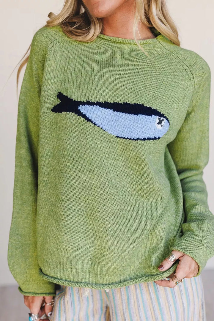 Pistachio green fish graphic sweater styled with striped pants, hand on hip