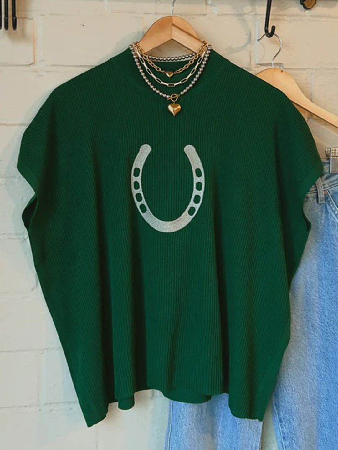 Dark green short sleeve sweater with horseshoe graphic hanging on a wooden hanger