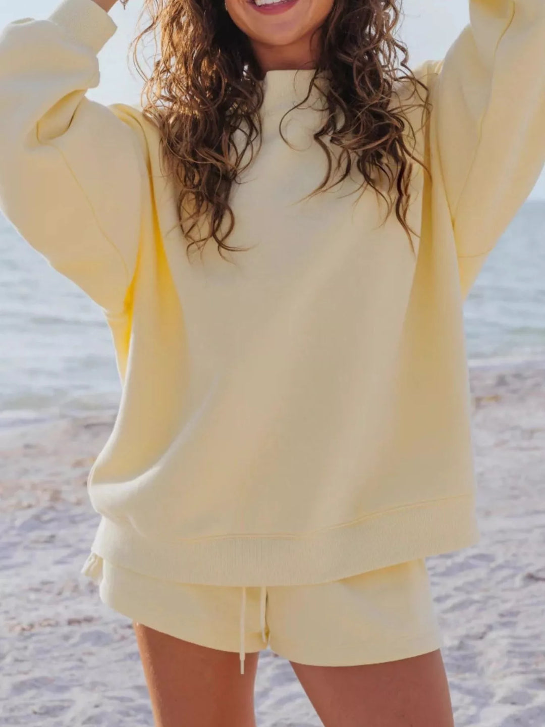 Butter yellow oversized sweatshirt and shorts set, arms stretched up on the beach