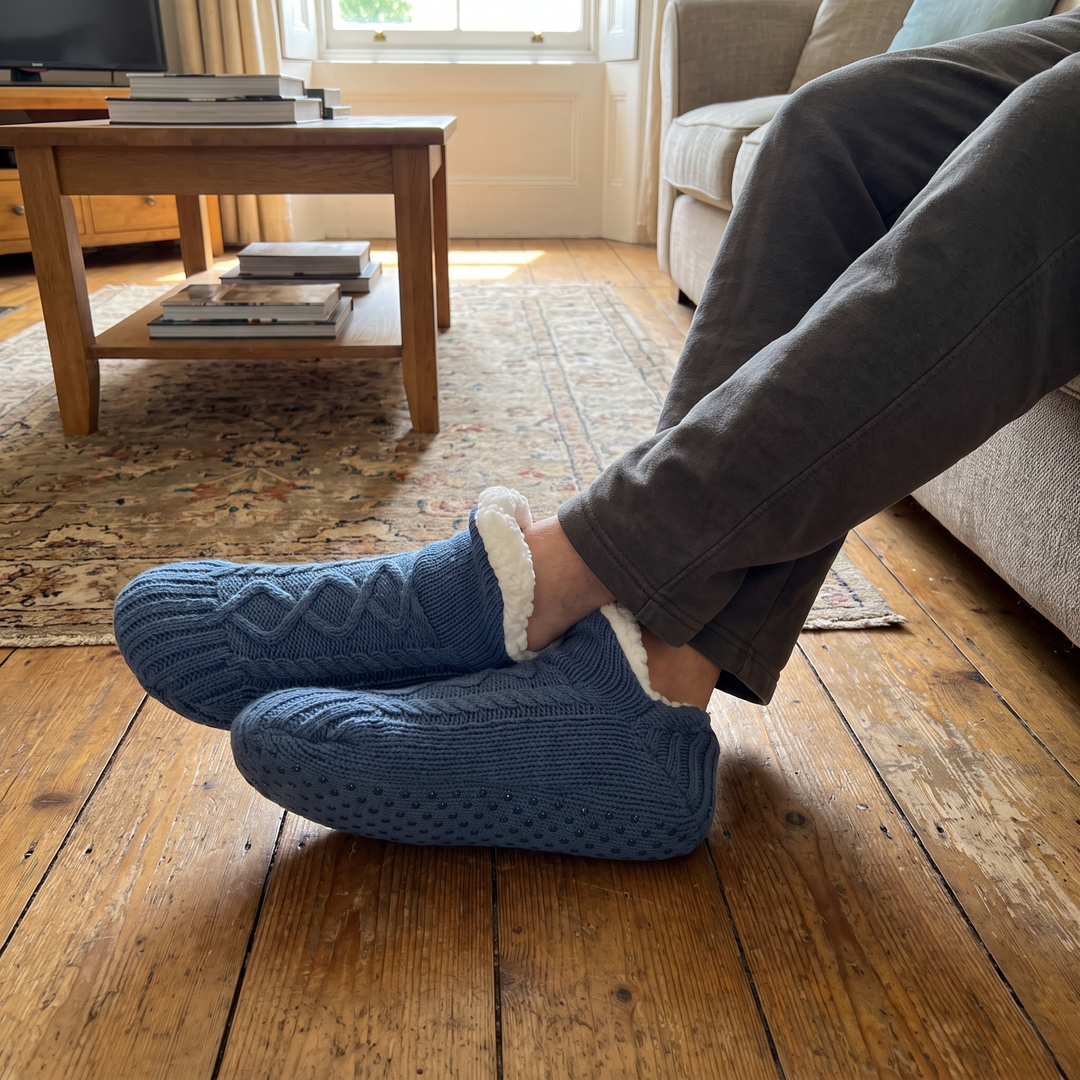 Blue slipper socks worn on a wooden floor in a living room
