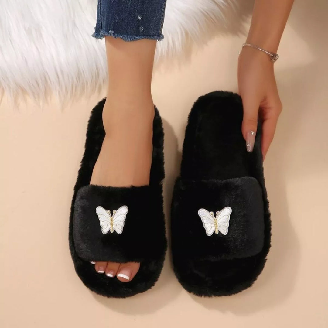 Women's slippers in black, fluffy open toe butterfly slide, worn on a peach floor