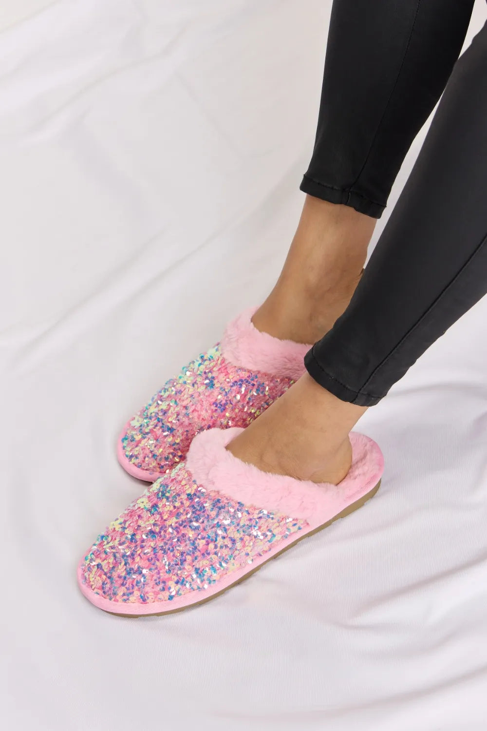 Pink closed toe sequin slippers seen from the side on a white blanket
