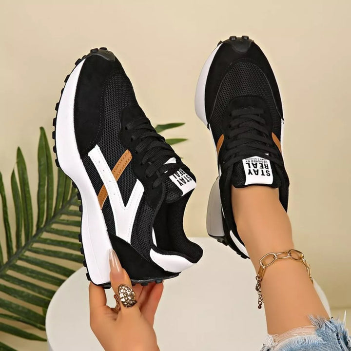 Black and brown platform sneakers with mesh panels, held beside palm leaves