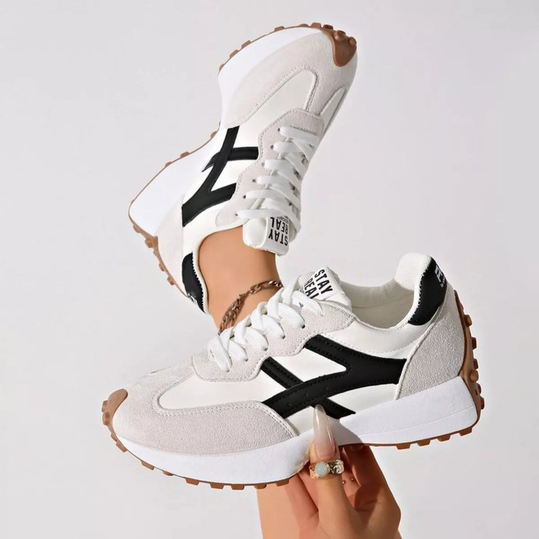 Light gray lace up sneakers with mesh panels and contrast stripe, held in hand