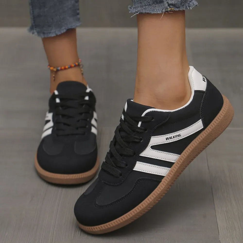 Women's sneakers in black, retro low top with white contrast stripes, worn with jeans