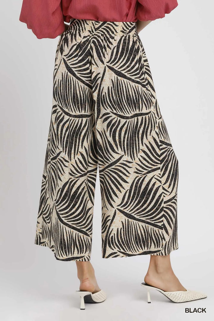 Back angle of the black palm print summer pants worn with white mules