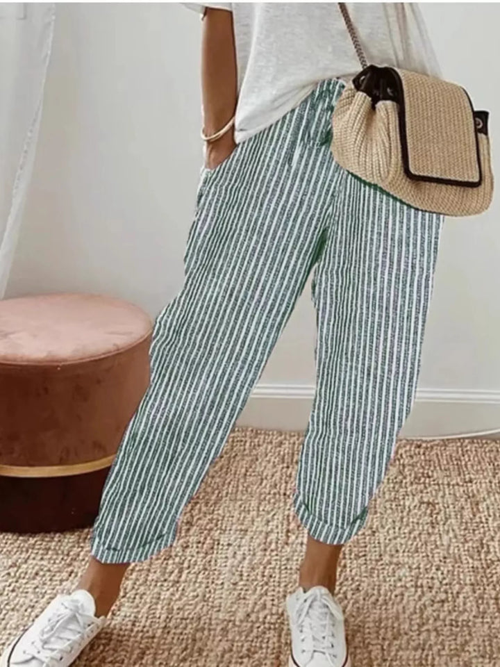 Green striped cropped summer pants worn with white sneakers and a woven bag