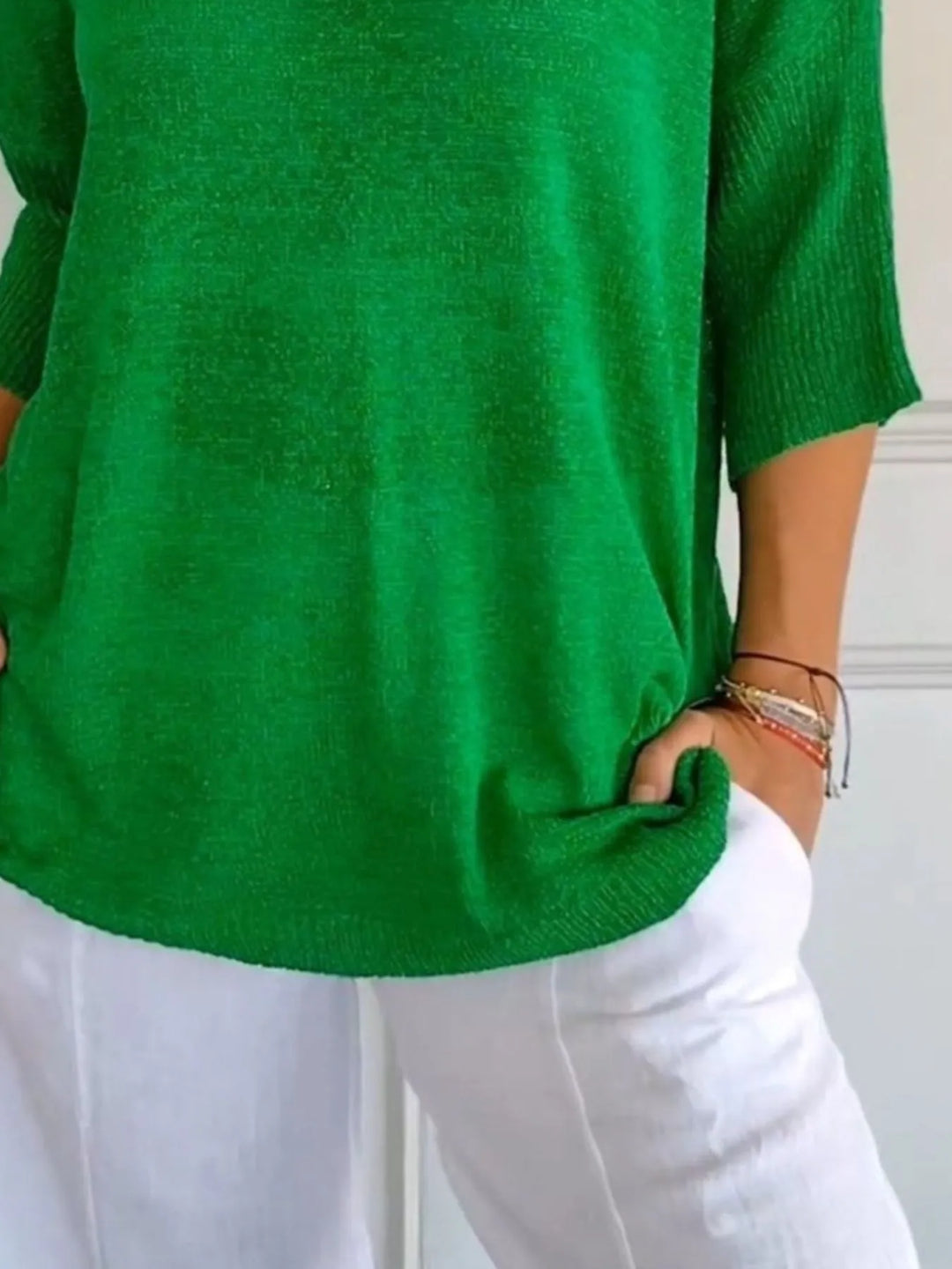 Green sweater close-up of the sleeve and relaxed hem over white pants