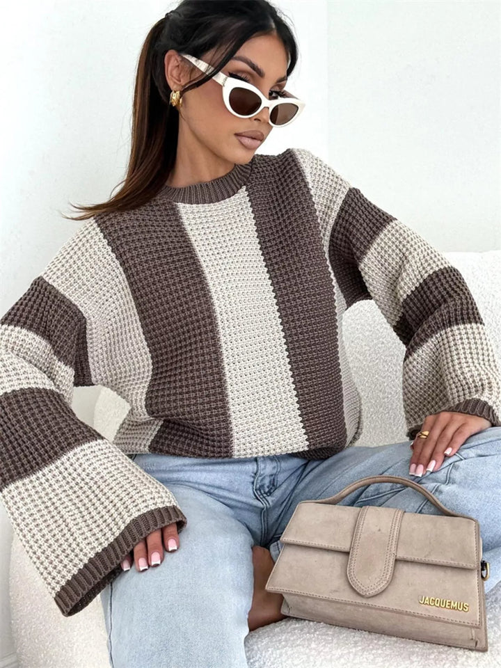Beige brown striped sweater with sunglasses, seated holding a taupe handbag