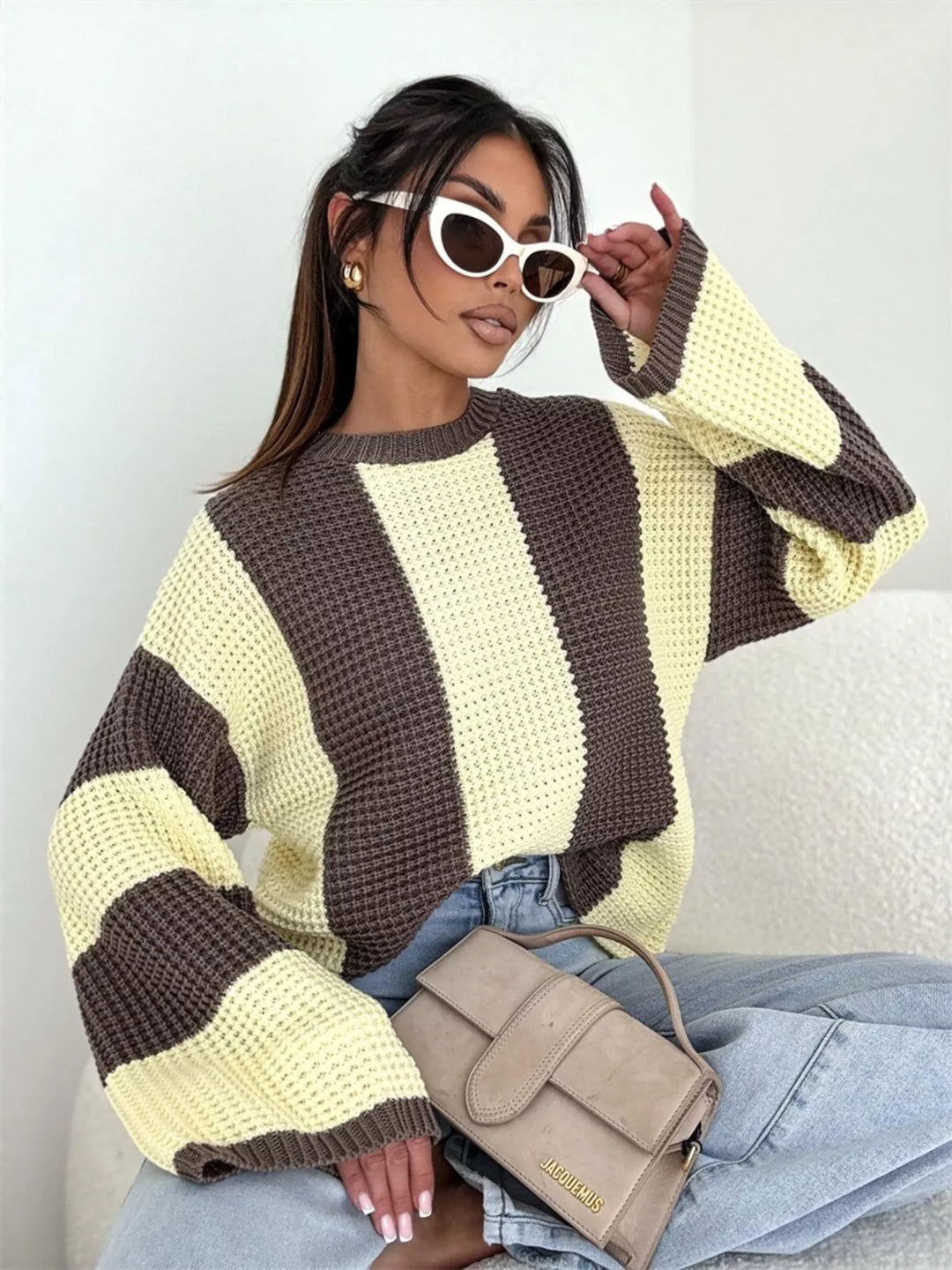 Yellow and brown striped sweater with wide sleeves, seated, styled with sunglasses and a handbag