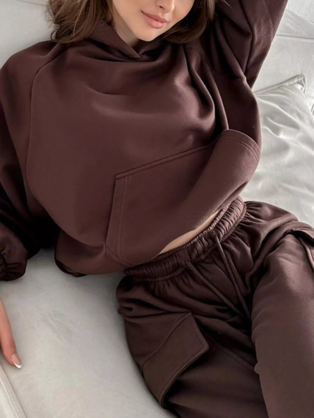 Brown hoodie pocket and jogger waistband, relaxed pose on a bed