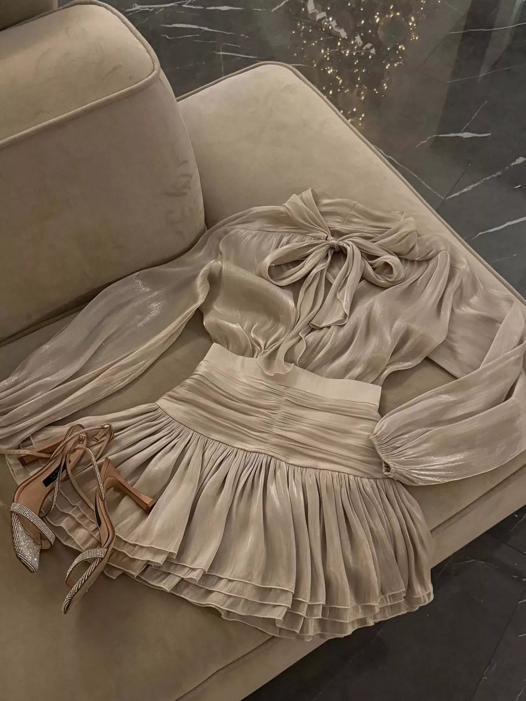 Flat lay of the champagne ruffle mini skirt with bow tie blouse on a sofa