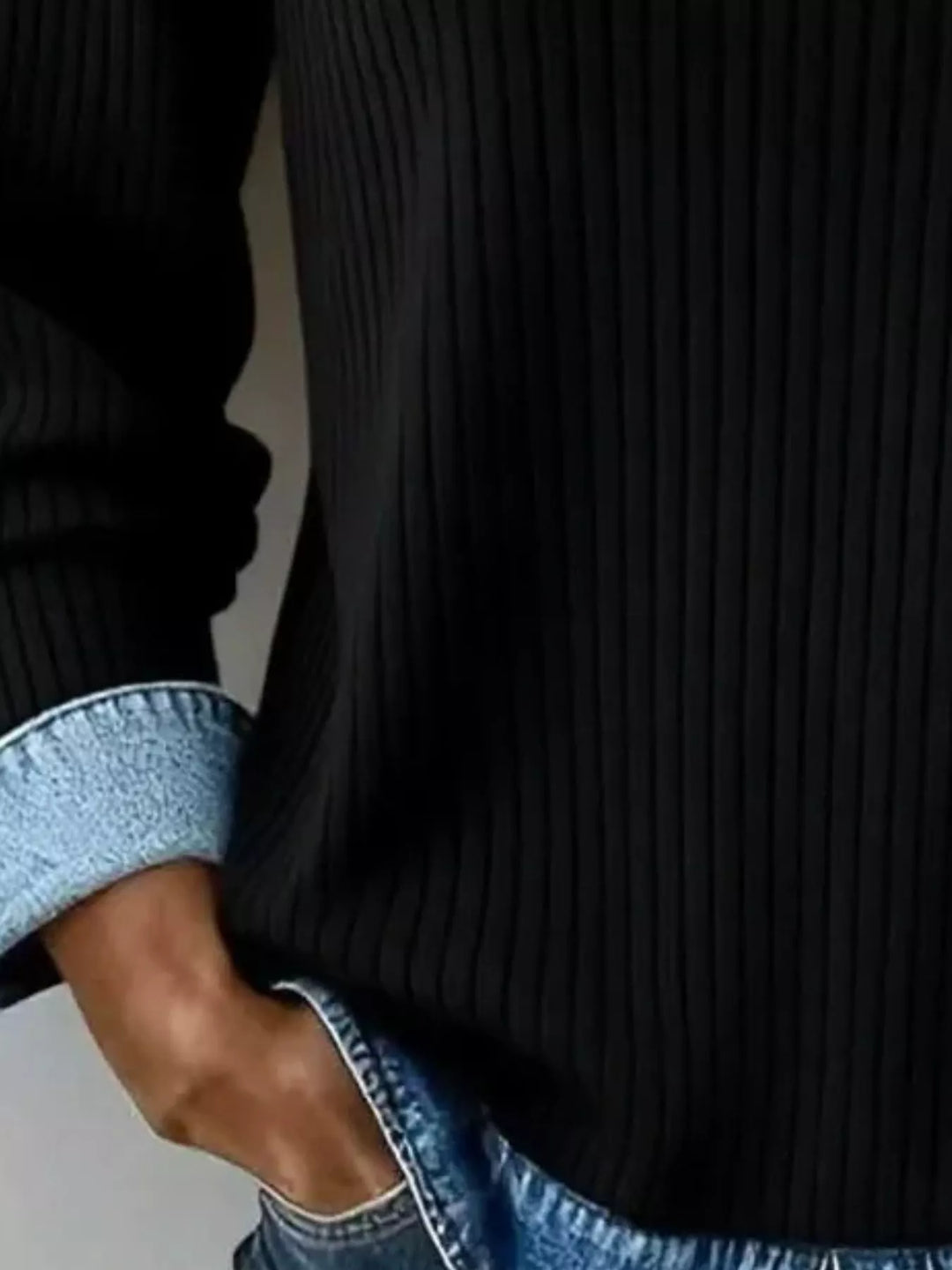 Close-up of the black ribbed knit sweater cuff and layered hem detail