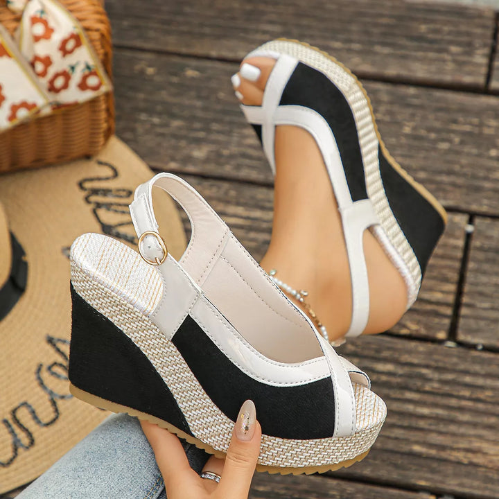 Black wedge sandals with buckled slingback strap, pair held in hand