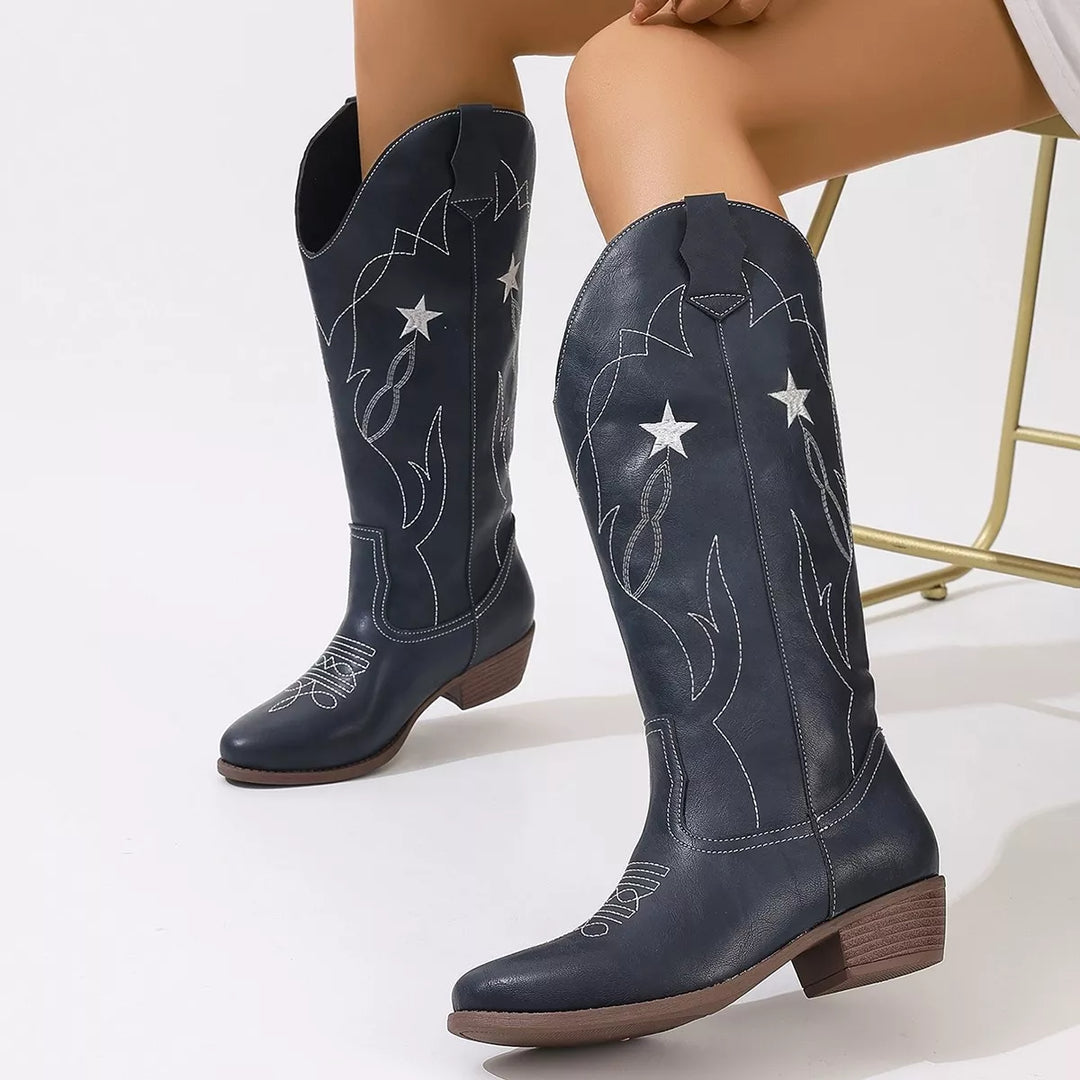 Pair of navy mid calf pull on boots standing on a white floor