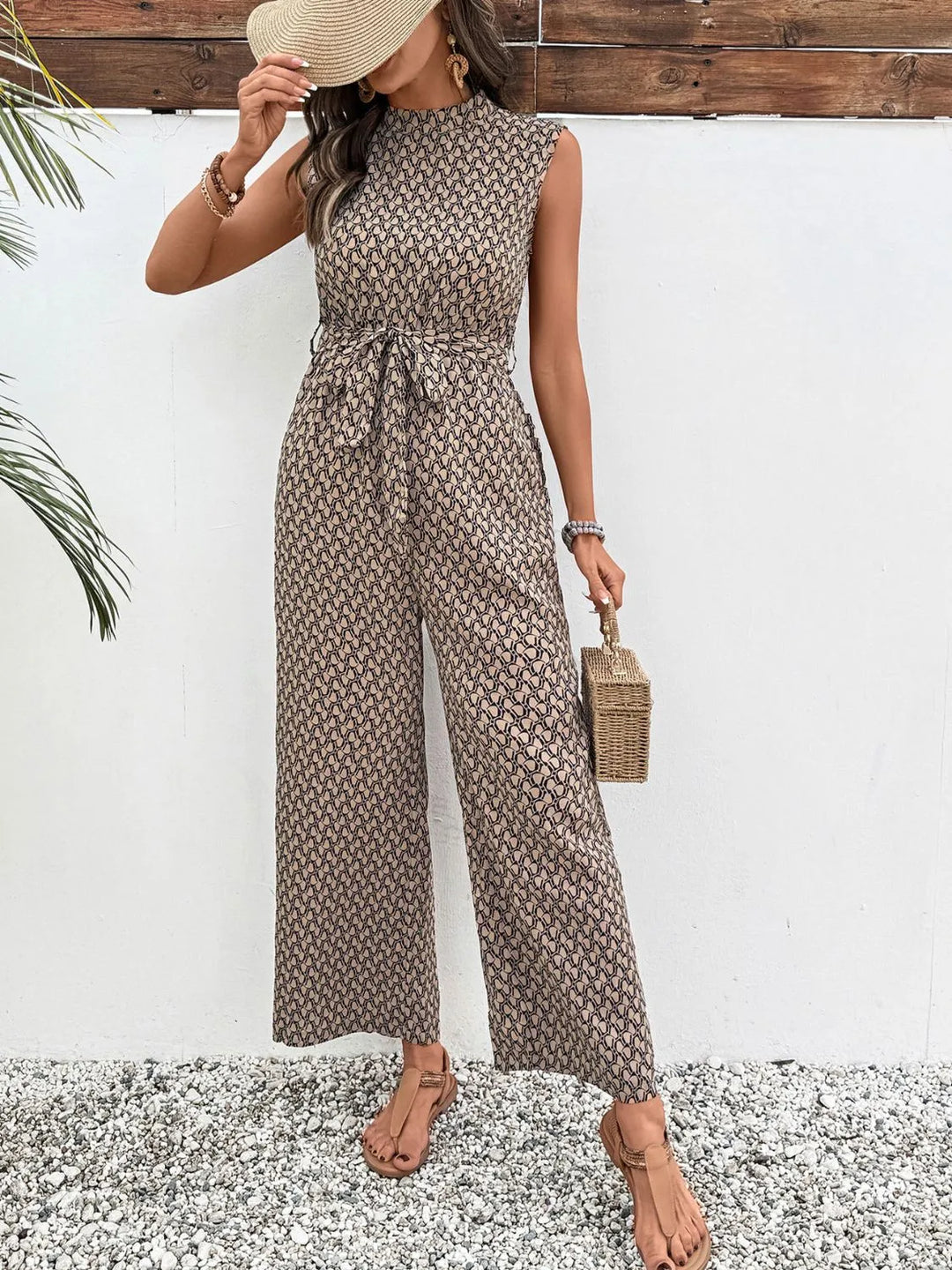 Taupe print mock neck jumpsuit worn with a sun hat held at the face