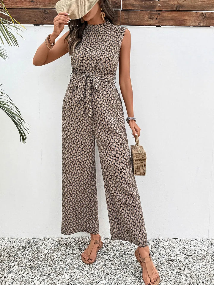 Taupe print mock neck jumpsuit worn with a sun hat held at the face