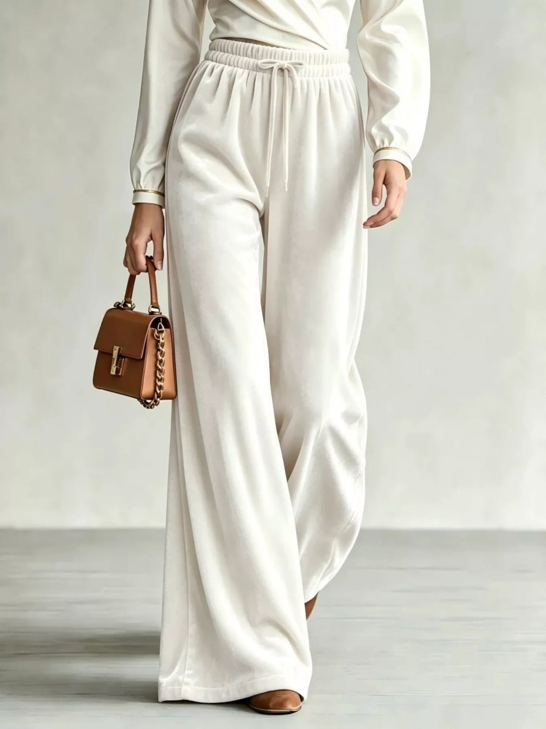 Ivory drawstring wide leg pants with velvet-look finish, walking with a tan bag
